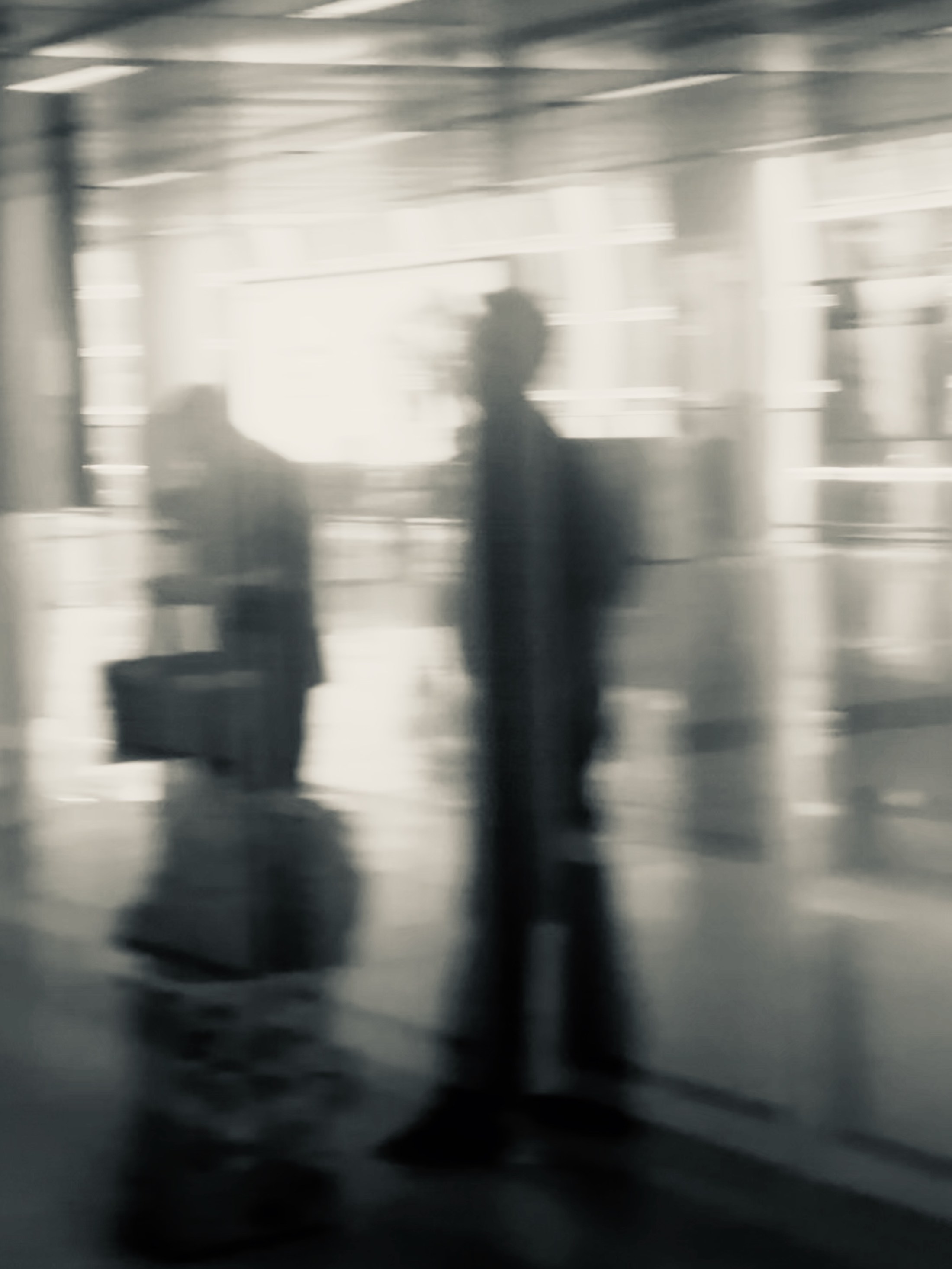 Blurred figures stretched between vertical bands of street architecture.